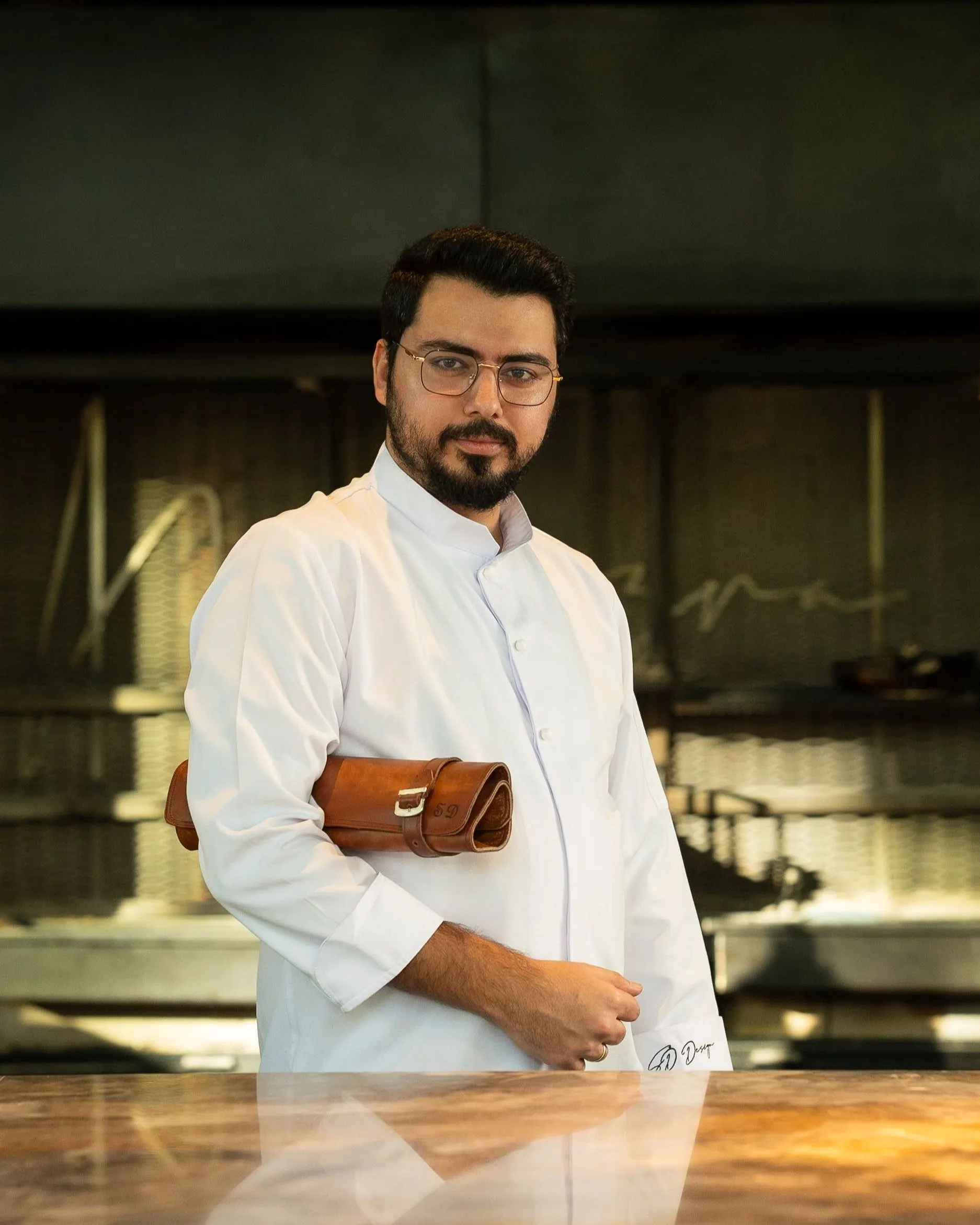 Serhat Doğramacı tezgâhın başında, kolunun altında deri bıçak çantasıyla