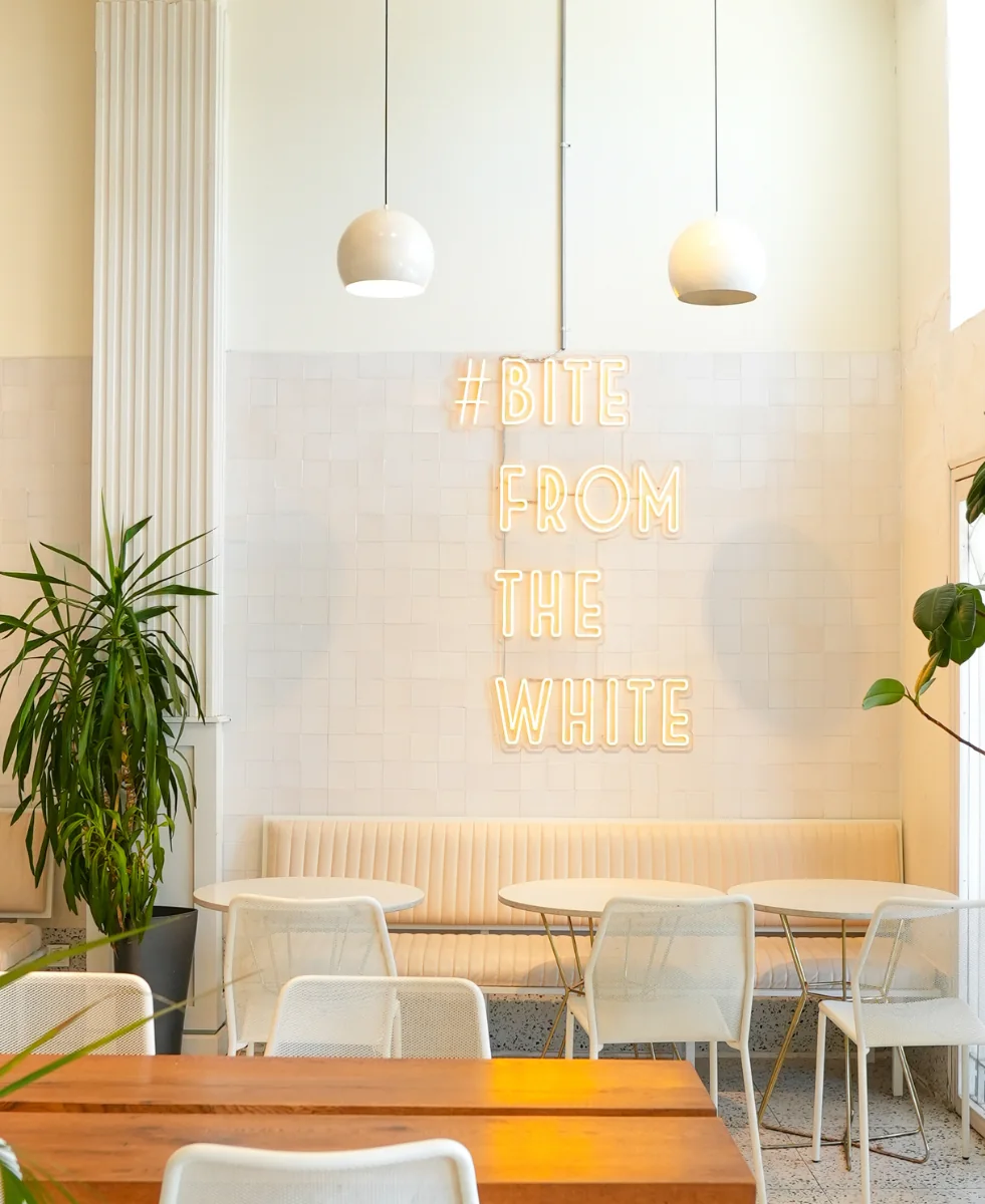 White Burger Yeniköy: a neon '#BITE FROM THE WHITE' on a white-tiled wall, pendant lamps, plants and a wooden table